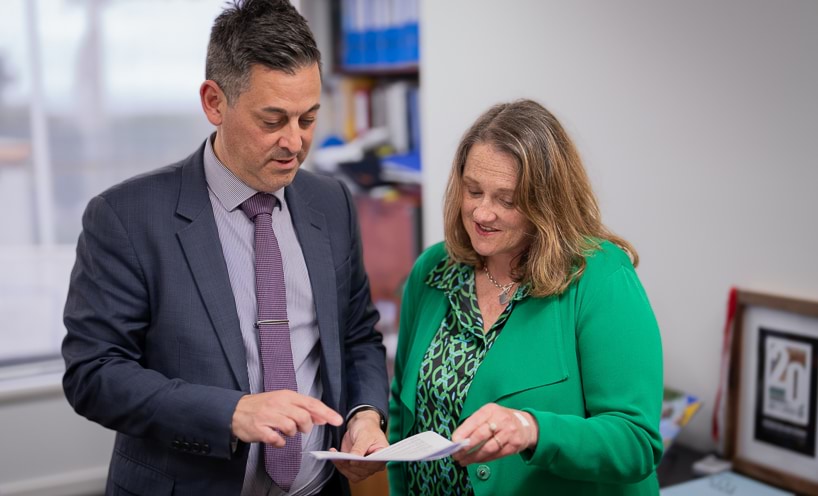 Two school staff point to and read a paper document.